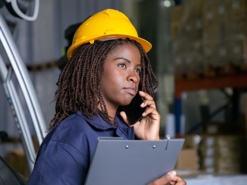 Une ingénieure au téléphone, concentrée, avec un casque de chantier jaune sur la tête.